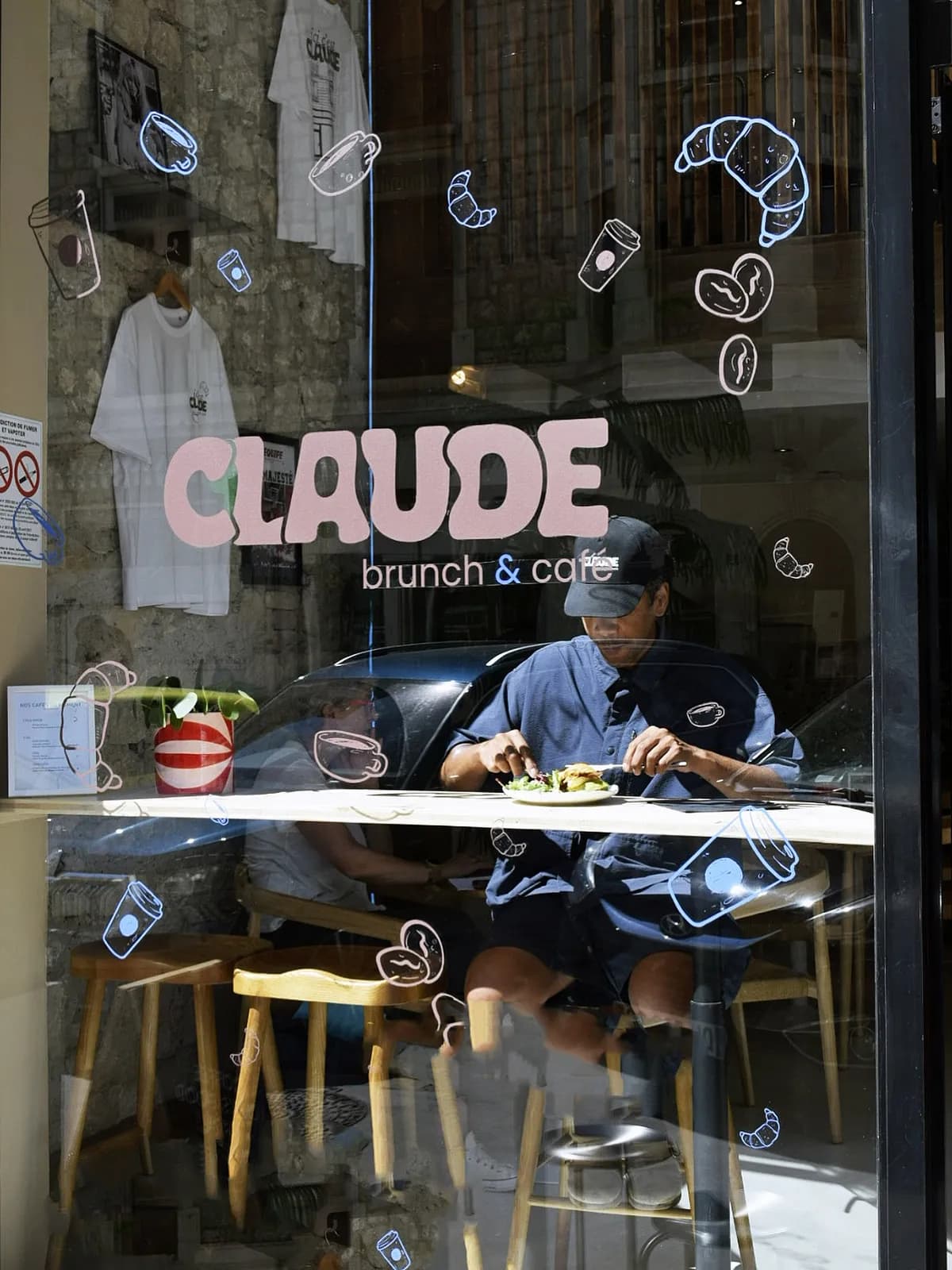 Vitrine de Claude à Annecy : logotype rose poudré et doodles dessinés sur la vitre, client attablé au comptoir